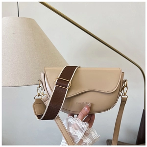 Close-up of a light beige saddle bag with logo detail and dual shoulder strap design