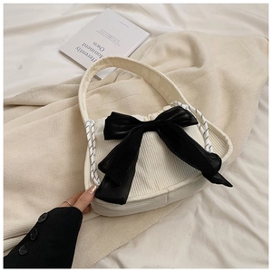 Detail of cream corduroy handbag featuring a large black bow and woven drawstring