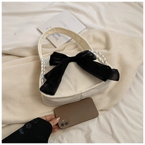 Close-up of white corduroy shoulder bag featuring a large black decorative silk bow detail