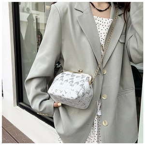 Detail of white evening bag with heart pattern and elegant gold chain strap