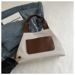 Close-up of beige canvas handbag with brown leather handles and decorative front pocket