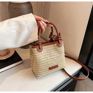 Detailansicht der Stroh-Eimertasche mit dunkelbraunen Ledergriffen und Markenlogo-Plakette