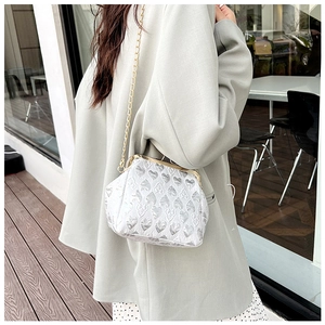 White heart-textured evening bag with gold chain shown on a model in a cafe setting