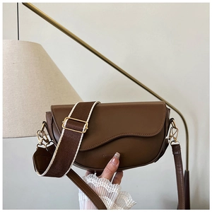 Detail of a brown leather saddle bag with wavy flap design and golden hardware finish