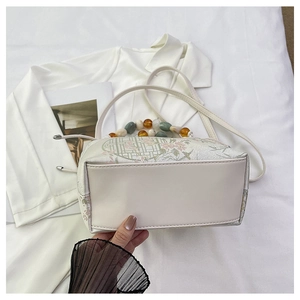 Gros plan sur la broderie florale et la poignée en perles colorées d'un sac à main beige