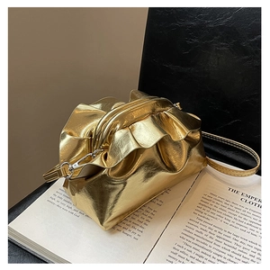 Detailed view of metallic gold ruched cloud bag on a book showing the sleek texture