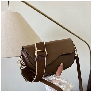 Detail of a brown saddle bag featuring adjustable wide woven strap and matte PU leather texture