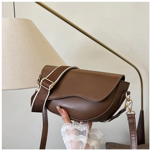 Detailed view of brown leather saddle bag featuring wavy flap and stylish woven strap