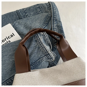 Detailed macro view of stitched faux leather handle on off-white canvas tote bag