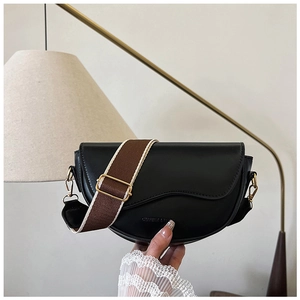 Detail of black saddle bag featuring golden logo and stylish wide fabric shoulder strap