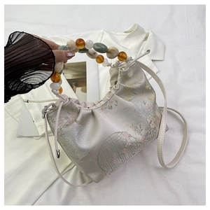 Détail de broderie florale et poignée en perles sur un sac à cordon de couleur crème