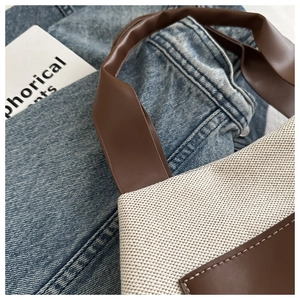 Detail of the stitching and handle connection on a white canvas and brown leather tote bag