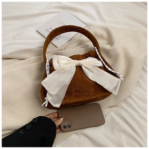 Detail of a brown corduroy handbag with a large white silk bow and braided rope strap