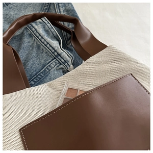 Detailed close-up of canvas tote bag with brown leather pocket and white contrast stitching