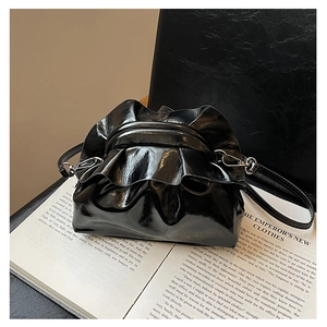 Detail of black glossy patent leather pleated cloud bag with silver metal hardware accents
