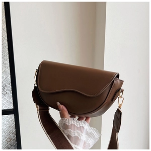 Close-up of brown leather saddle bag with wavy flap and dual-tone wide woven strap