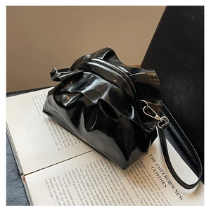 Detail of a black glossy pleated dumpling bag featuring a classic metal frame closure