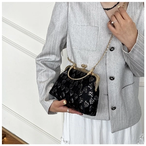 Detail of a black heart-embossed evening bag with gold metal frame and chain strap