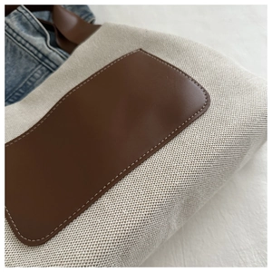 Detail of canvas tote bag showing dark brown leather pocket and stitching texture
