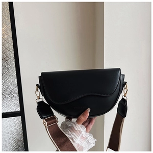 Close-up of black saddle bag with textured flap and striped woven shoulder strap