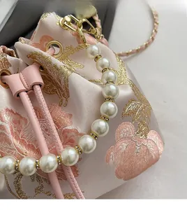 Detailed close-up of pink satin bucket bag with floral embroidery and pearl handle