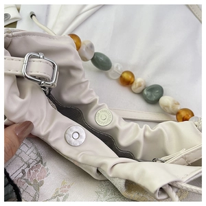 Détail du sac à main plissé beige avec fermoir magnétique et chaîne de perles en pierre
