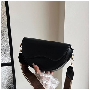 Detail of black saddle bag with wavy flap edge and wide brown textile strap