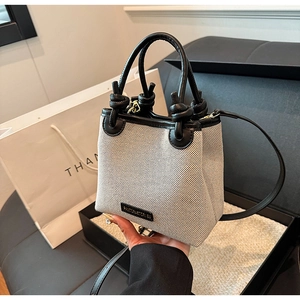 Detailaufnahme der beigen Strohtasche mit schwarzem Lederbesatz und Markenlogo
