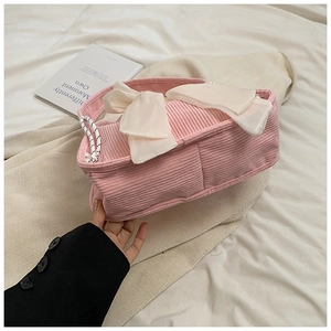 Detail of pink corduroy handbag featuring a large white bow and sleek drawstrings