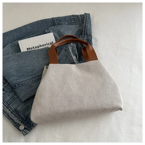 Detail view of cream canvas tote bag with brown leather handles on denim background