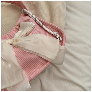 Close-up of pink corduroy handbag featuring a large white satin bow and woven strap