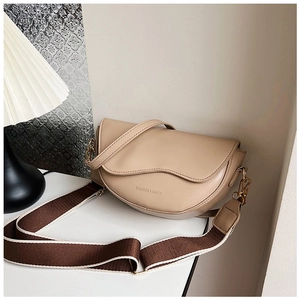 Detail of beige saddle bag with wavy flap and adjustable brown fabric shoulder strap