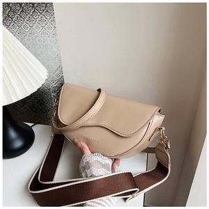 Detail of beige saddle bag with wide woven strap and gold hardware on white table