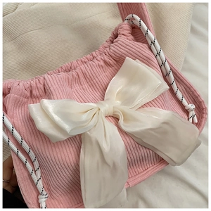 Close-up of pink corduroy handbag with a large white satin bow and woven straps
