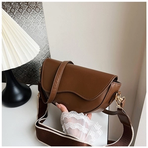 Detail of a dark brown leather half-moon saddle bag with wavy flap and golden hardware
