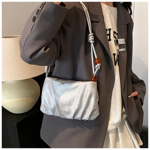 Detalle de bolso plisado plateado con textura metálica y cuentas naranjas en la correa