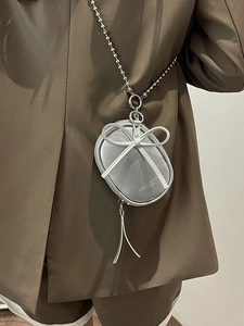 Mini bolso bandolera plateado con lazo y borla llevado por modelo en traje elegante