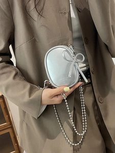 Mini bolso ovalado plateado con lazo metálico y cadena de cuentas en atuendo de moda