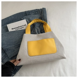 Close-up of a white canvas bucket bag with yellow leather pocket and handle details