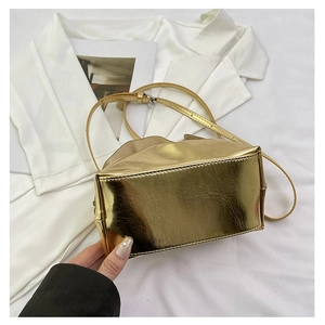 Close-up of golden mirror finish shoulder bag with adjustable strap and textured pleats