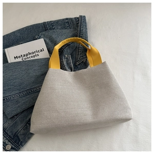 Detail of white knitted bucket bag with contrast yellow handle on casual denim backdrop