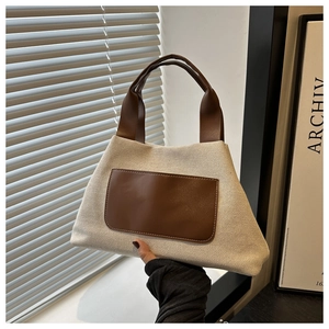 Detailed view of beige canvas handbag with brown leather pocket and white stitching accents