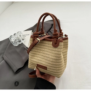 Detail der Strohtasche mit braunem Lederbesatz und Schultergurt auf grauem Blazer