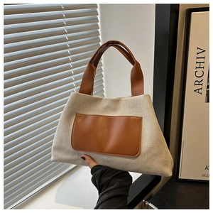 Detail of canvas tote bag featuring brown leather pocket and textured beige fabric