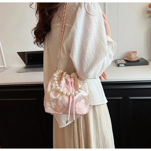 Detail of pink floral embroidery bucket bag featuring a pearl handle and chain strap