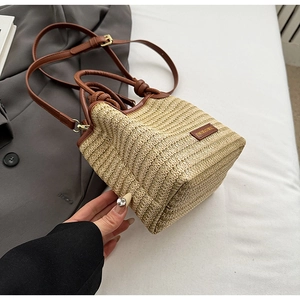 Detailansicht der Stroh-Eimertasche mit braunem Lederbesatz und Metall-Markenlogo
