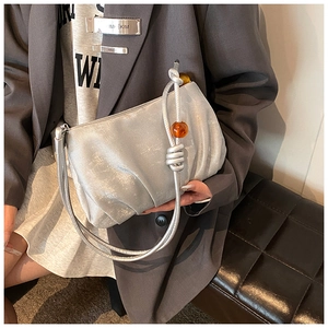Detalle del bolso nube plateado plisado con textura metálica y cuenta naranja en la correa
