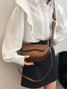 Classic brown saddle crossbody bag with adjustable straps on elegant model outfit