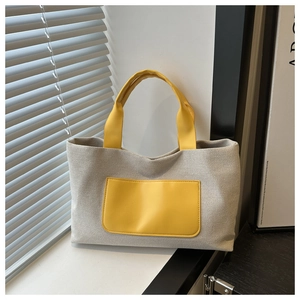 Detailed close-up of a canvas tote bag with a bright yellow leather pocket on a window sill