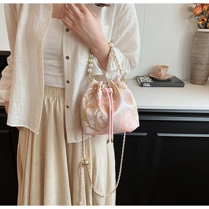 Detailed view of pink satin bucket bag with golden floral embroidery and pearl handle